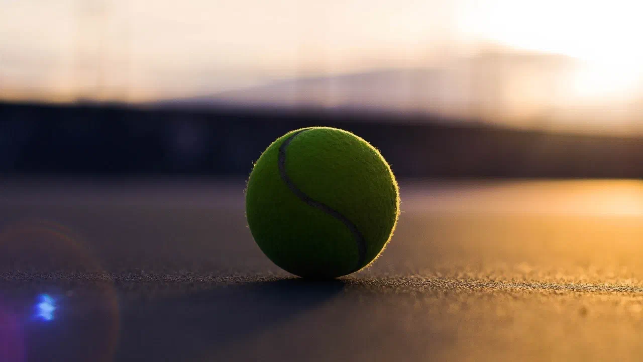 A tennis ball resting on a hard court at sunset